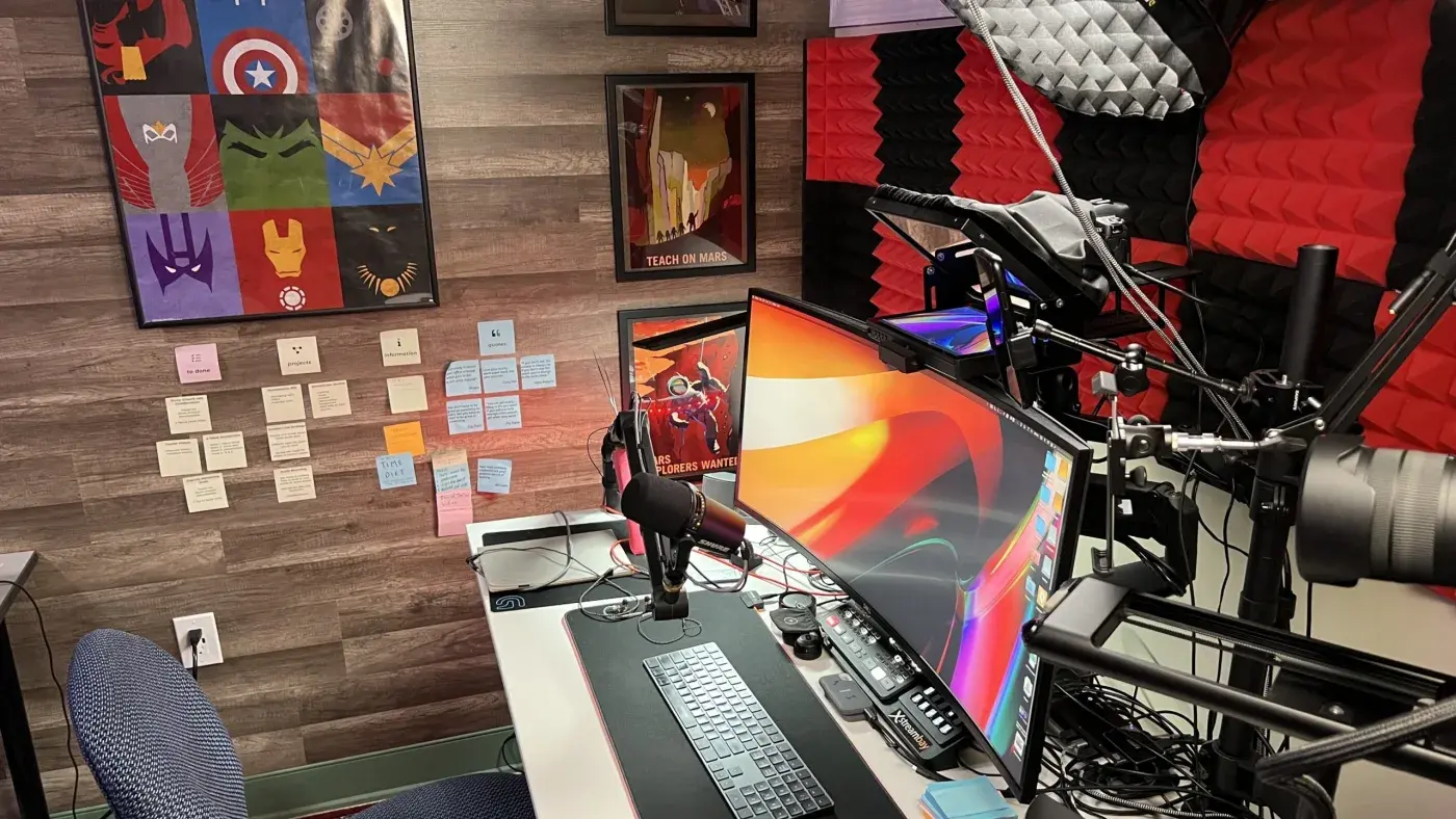 A finished, professionally lit home studio with a podcast mic, curved monitor, and acoustic treatment.